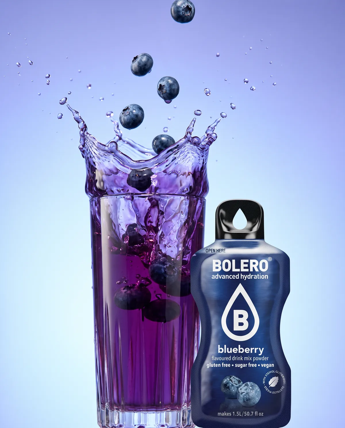 Glas mit violettem Heidelbeer-Drink, Splash mit fliegenden Blaubeeren, daneben das Bolero-Päckchen Blueberry