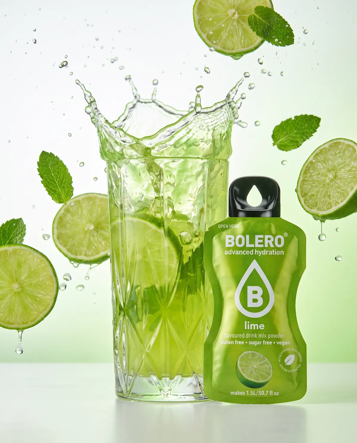 Glas mit grünem Limetten-Drink, Splash mit Limettenscheiben und Minze, daneben das Bolero-Päckchen Lime