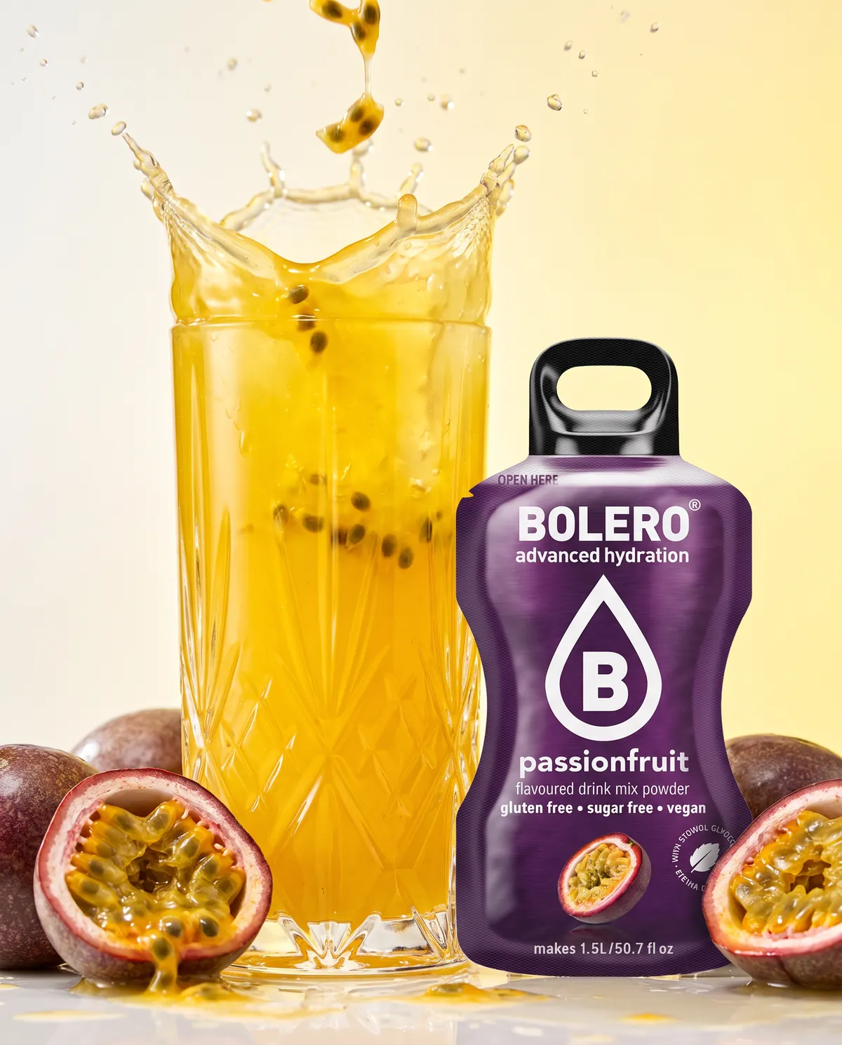 Glas mit gelbem Passionsfrucht-Drink, Splash mit halbierten Passionsfrüchten, daneben das Bolero-Päckchen Passionfruit
