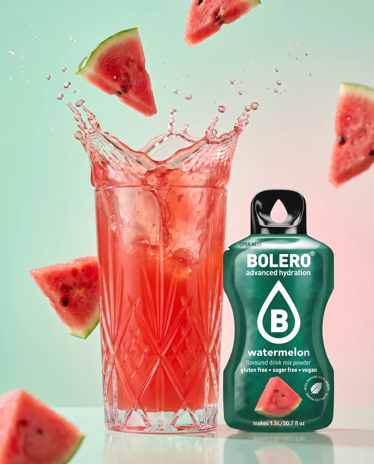 Glas mit rotem Wassermelonen-Drink, Splash und fliegende Melonenstücke, daneben das Bolero-Päckchen Watermelon